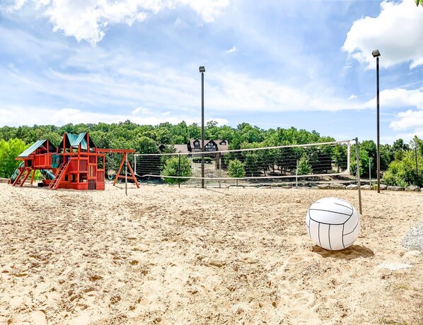 A sandy beach volleyball court with a net, a volleyball, and a red play structure.