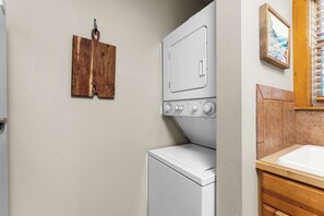 A laundry room with a white washer and dryer, wooden wall-mounted towel racks, and a wooden cabinet with a sink. - Cedar Ridge Cabin, Stonebridge Village (Branson West)