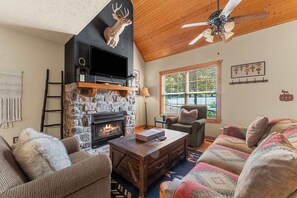 A cozy living room with a stone fireplace, a television, and a ceiling fan.