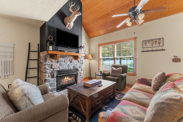 A cozy living room with a stone fireplace, a television, and a ceiling fan.