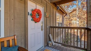 A wooden porch with a white door, a red wreath, and a bench. - Cedar Ridge Cabin, Stonebridge Village (Branson West)