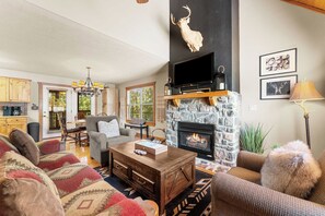 A cozy living room with a stone fireplace, a television mounted above it, and a comfortable seating area with a patterned rug.