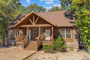 A two-story lodge with a wooden exterior, a porch with a staircase, and a stone foundation.