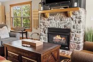 A cozy living room with a stone fireplace, a television mounted above it, and comfortable seating.