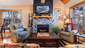 A cozy living room with a stone fireplace, a mounted deer head, and a television displaying 'NIGHTLY VACATIONS'. - Cedar Ridge Cabin, Stonebridge Village (Branson West)