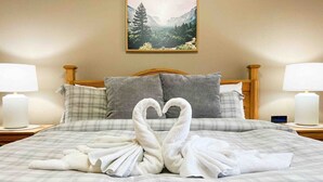 Une chambre d’hôtel avec un lit agrémenté d’un tableau représentant un paysage de montagne, deux lampes de chevet et une décoration en forme de cœur réalisée avec des serviettes.