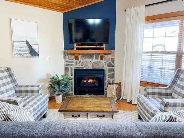 A living room with a stone fireplace, a flat-screen TV mounted above it, and two plaid armchairs. - Branson Cabin with Two Master Suites! (Branson West)