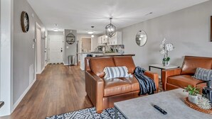 A modern living room with a brown leather sofa, a coffee table, and a kitchen in the background. - Renovated Luxury! Indoor and Outdoor Pools! (Branson)