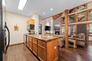 A spacious living area with a wooden floor, a stone fireplace, and a large window with blinds.