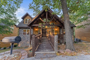 A two-story log cabin with a stone foundation, a wooden deck, and a mailbox.