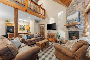 A cozy living room with a fireplace, a stone wall, a wooden staircase, and a kitchen in the background. - ONE MILE to Silver Dollar City! Rustic Cabin! (Branson)