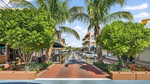 A street lined with palm trees and buildings, with a sidewalk and a road in the center. - Oceanfront Condo Located in Paradise on S. Hutchinson Island/Stuart 
 (Stuart)