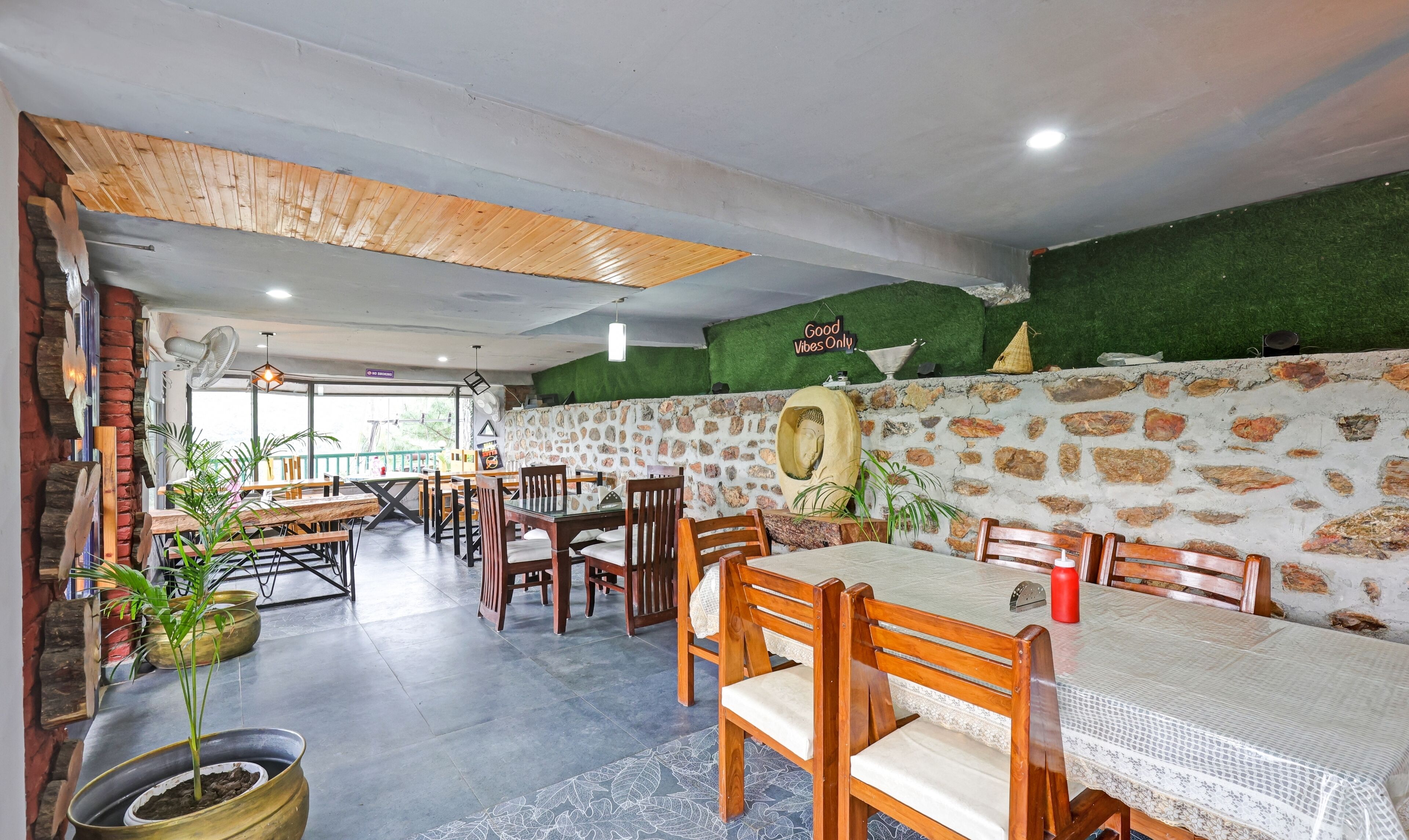 Un restaurante con mesas y sillas de madera, paredes de piedra y césped artificial verde.