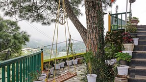 A stone staircase with white potted plants, a wooden swing, and a view of a lake and buildings in the distance. - Treebo Vista Lago With Lake View (Nainital)
