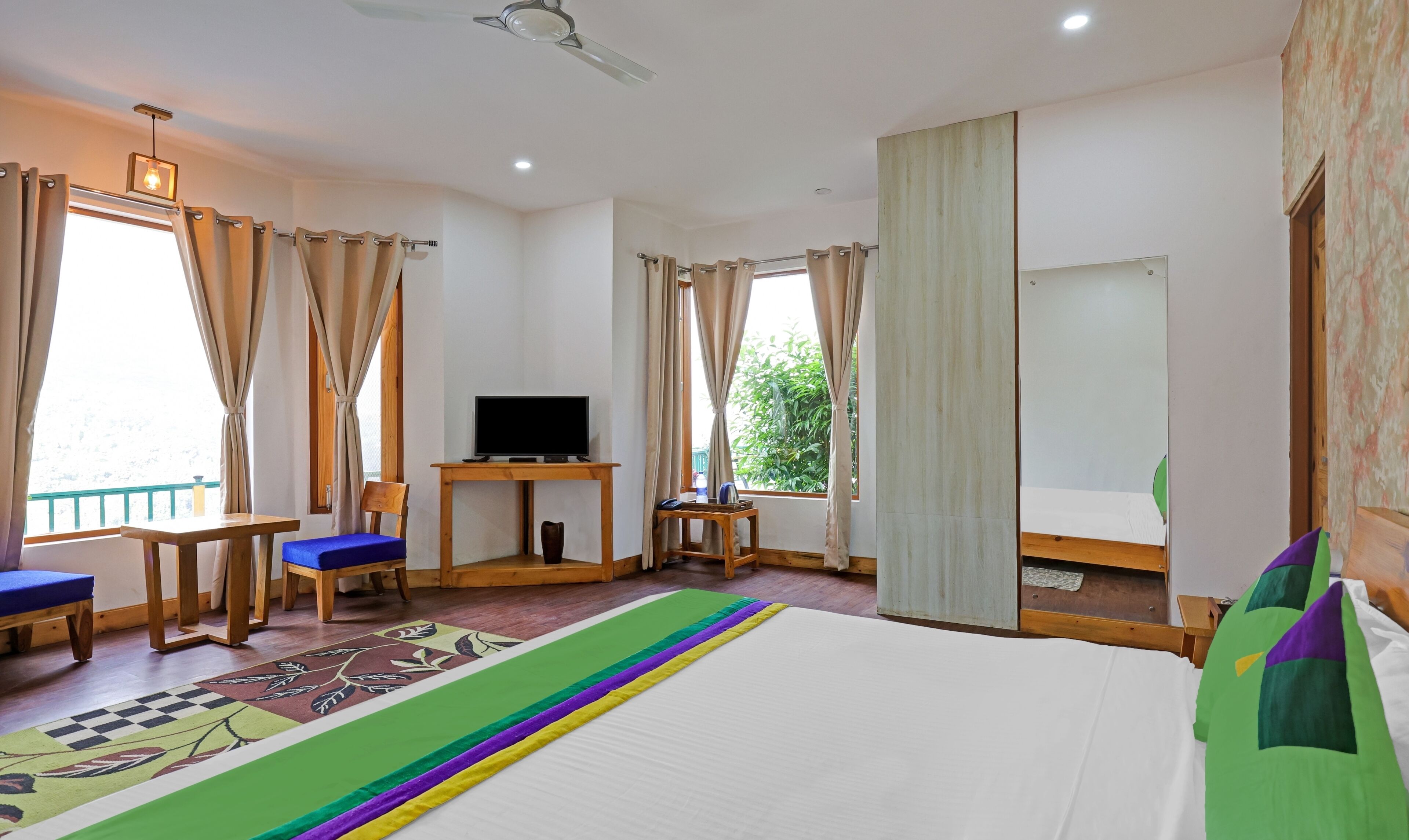 A hotel room with a bed, a desk with a TV, a chair, and a window with curtains.