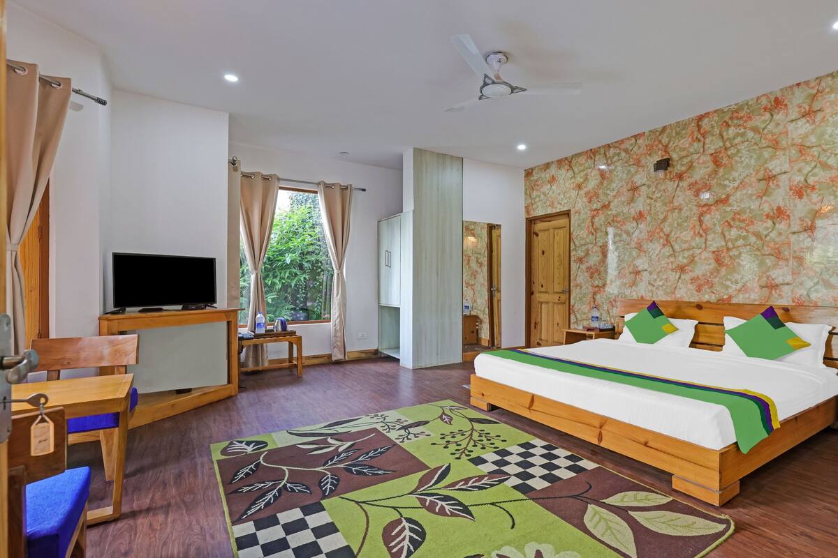 A bedroom with a bed, a TV, a desk, and a window with curtains.