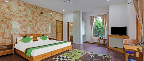 A bedroom with a bed, wooden nightstands, a TV, a desk, and a window with curtains.