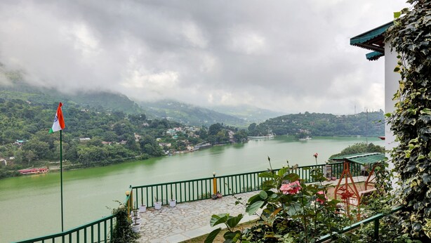 A riverside view with a flag, a stone-paved area, and greenery. - Treebo Vista Lago With Lake View (Nainital)