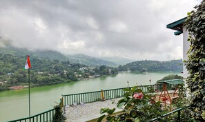A riverside view with a flag, a stone-paved area, and greenery. - Treebo Vista Lago With Lake View (Nainital)