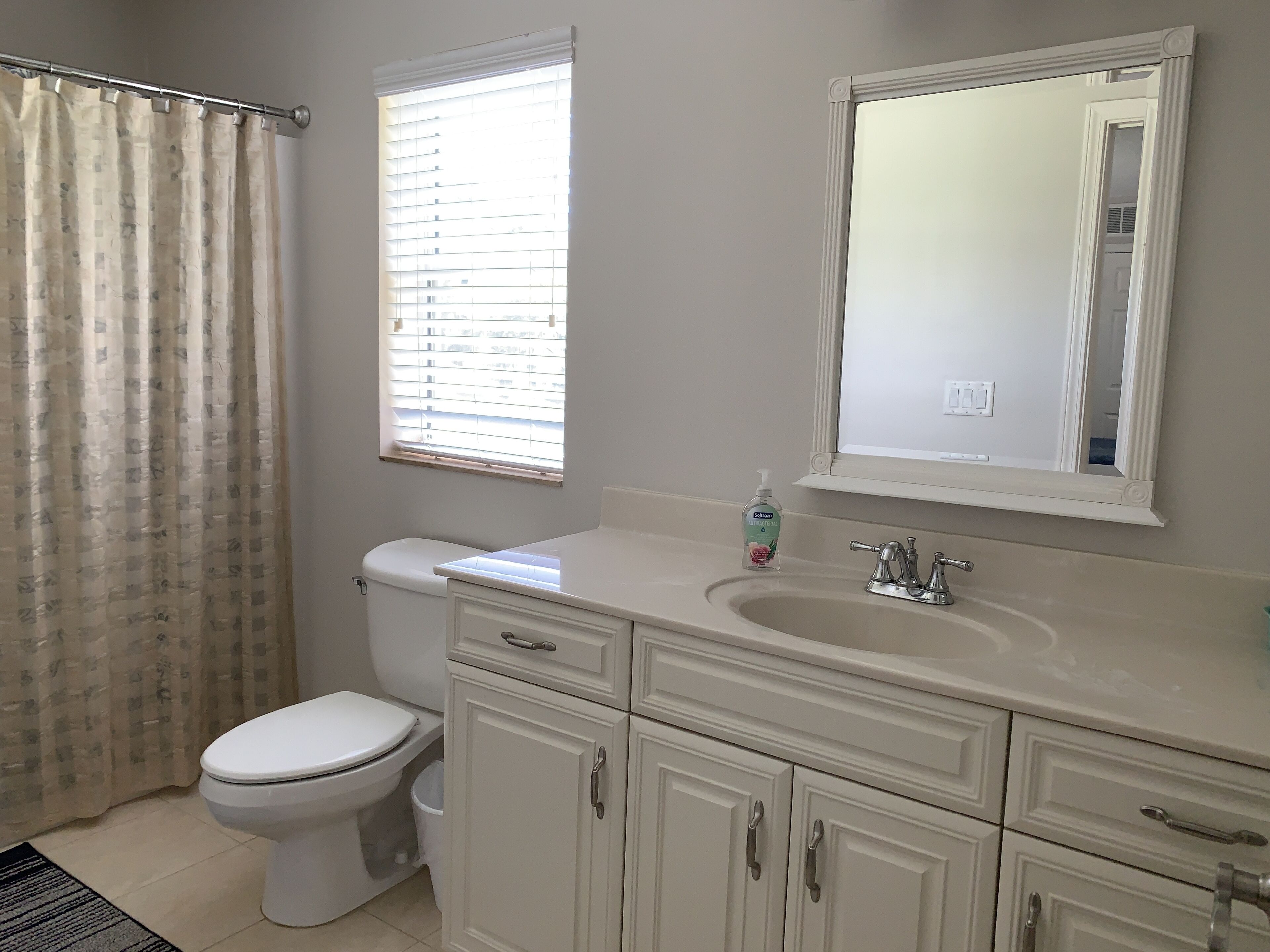 A bathroom with a toilet, a sink, a mirror, and a window with blinds.