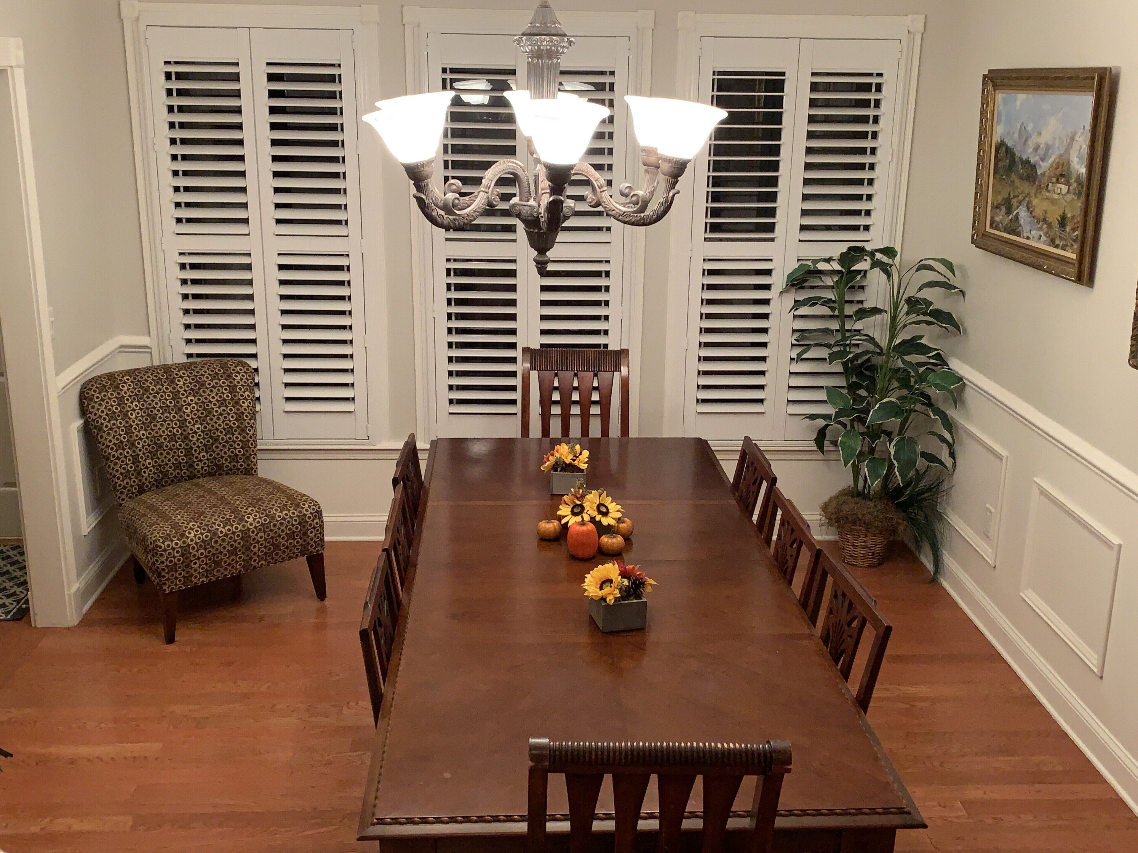 A dining room with a wooden table, patterned chairs, a chandelier, and a painting on the wall.
