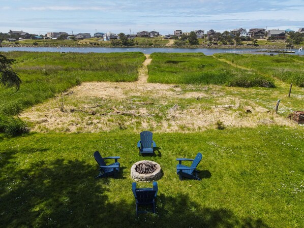A grassy outdoor area with four Adirondack chairs and a fire pit.