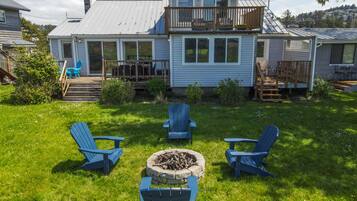 A house with a deck, a fire pit, and four Adirondack chairs in the yard.