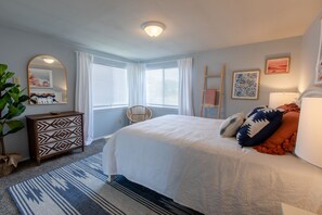 A bedroom with a large bed, a dresser, a chair, and a mirror.