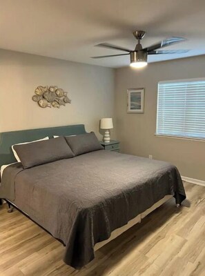 A bedroom with a bed, a ceiling fan, a nightstand with a lamp, a wall clock, and a window with blinds. - Close to beach & Steps to pool = AMAZING VACATION! (Miramar Beach)
