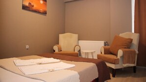 Habitación de hotel con cama, dos sillones, una mesita y un cuadro en la pared.
