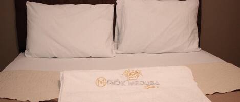 A neatly made bed with white linens, a brown headboard, and a towel with a logo on it.
