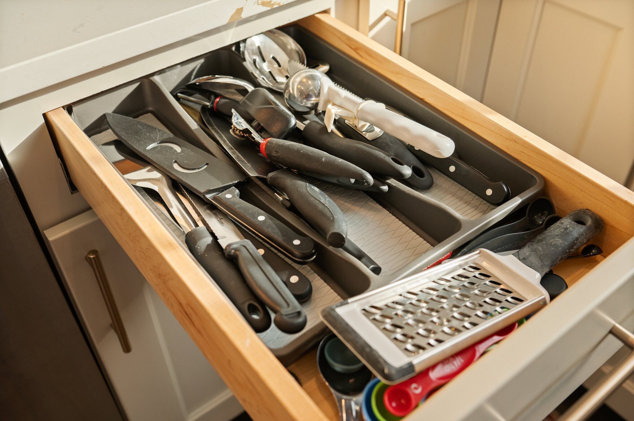 Un cajón de cocina con varios utensilios, entre ellos cuchillos, un rallador y una cuchara.