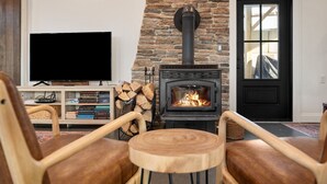 A cozy living room with a stone fireplace, a television, and wooden furniture. - Spacious Winter Retreat w/ Hot Tub, Games, Fire Pit & Scenic Hilltop Views! (Thompson)