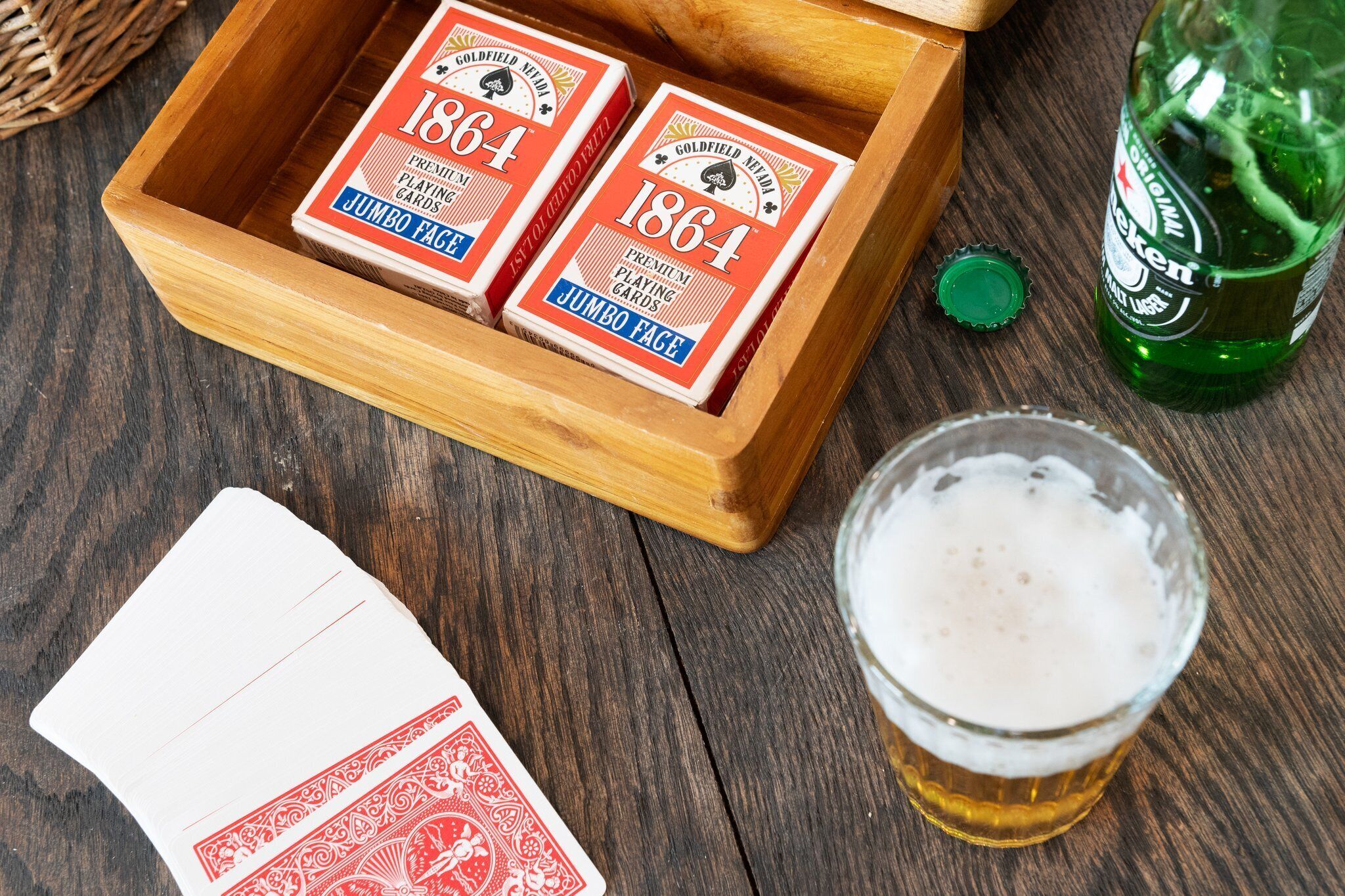 Una caja de madera con cartas, una botella de cerveza entreabierta y un vaso de cerveza sobre una superficie de madera.