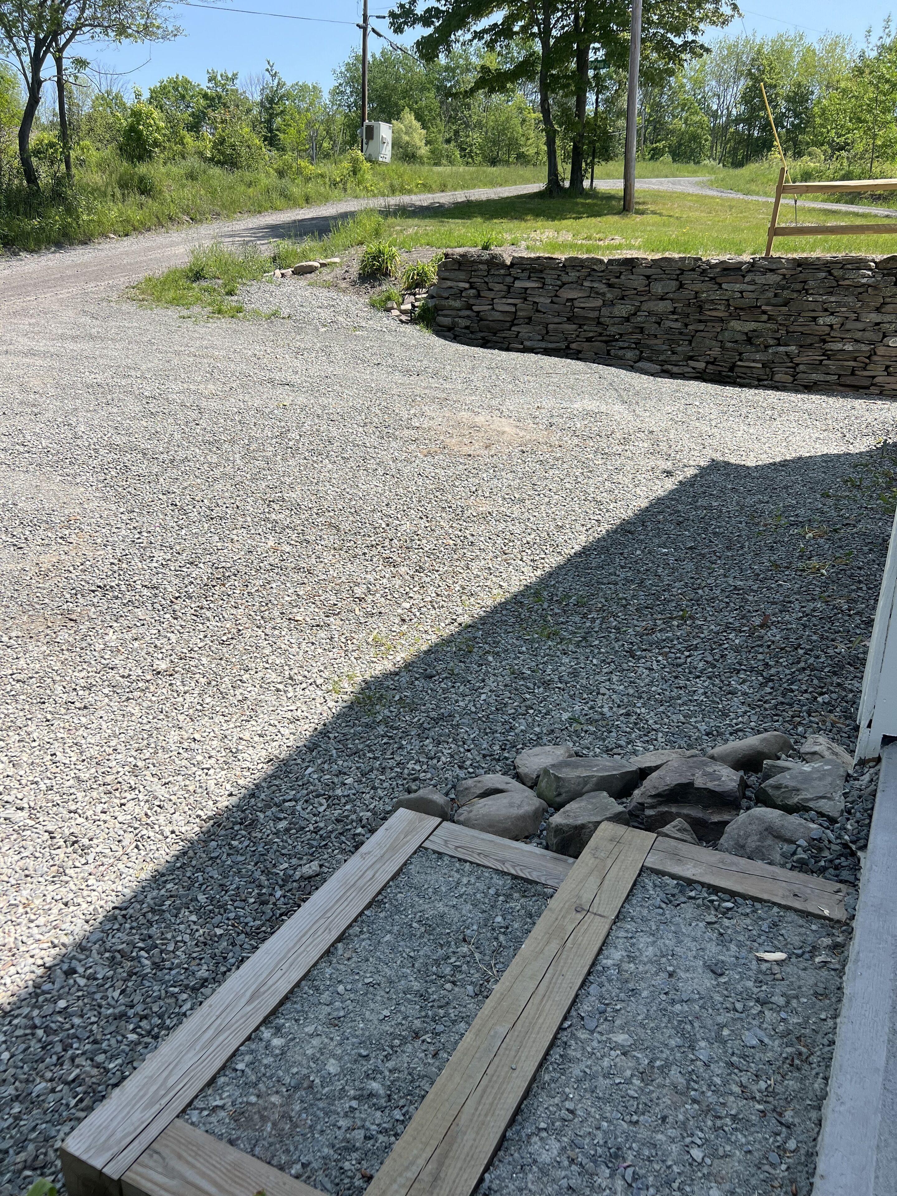 A gravel driveway leading to a stone wall and wooden deck.