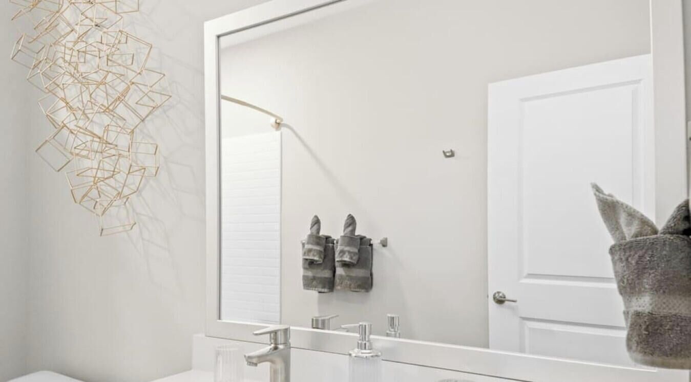 A modern bathroom with a large mirror, a white sink, and two towels hanging on the wall.