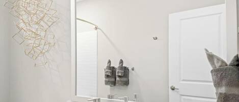 A modern bathroom with a large mirror, a white sink, and two towels hanging on the wall.