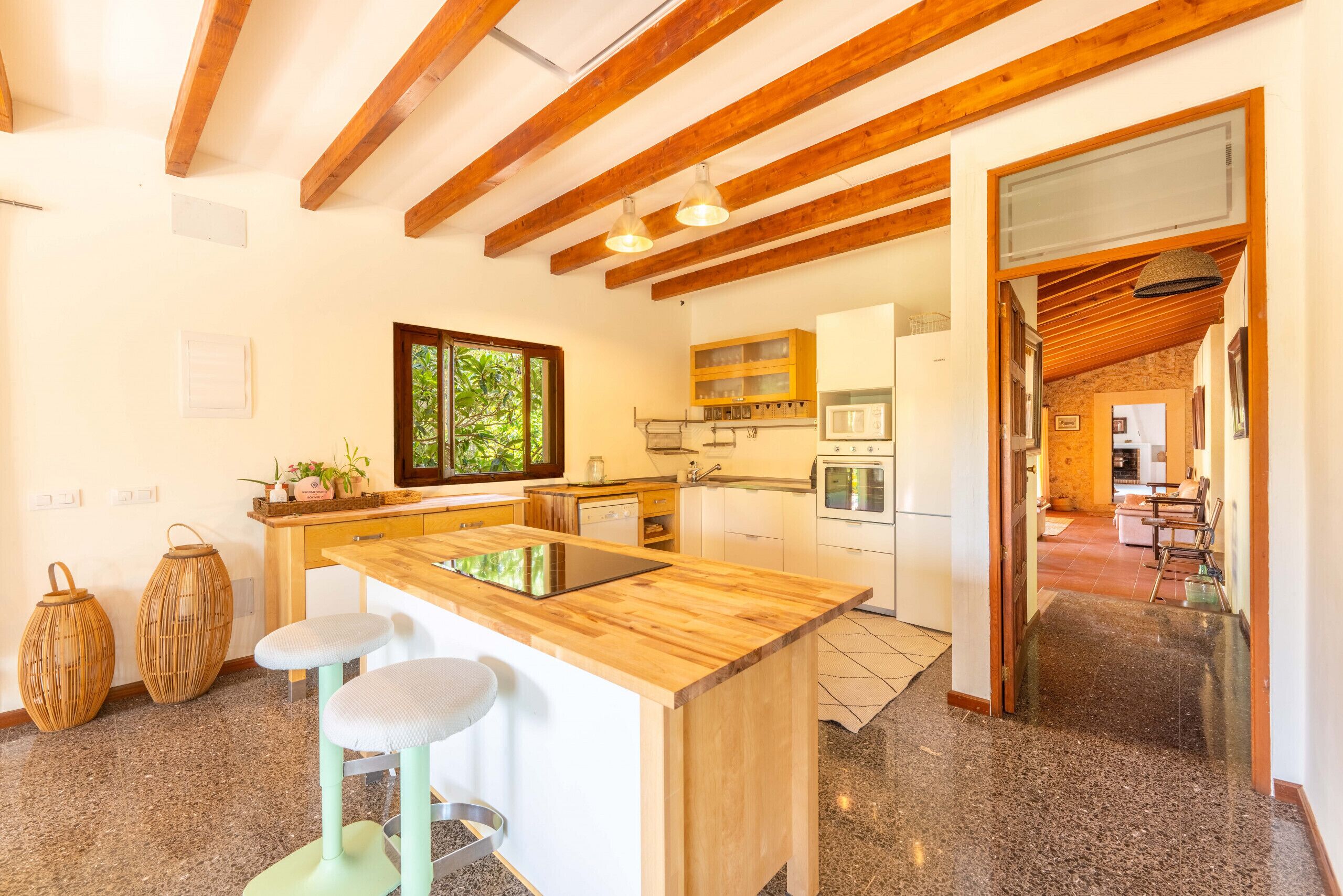 A modern kitchen with wooden beams, a central island, bar stools, and a view of the outdoors.