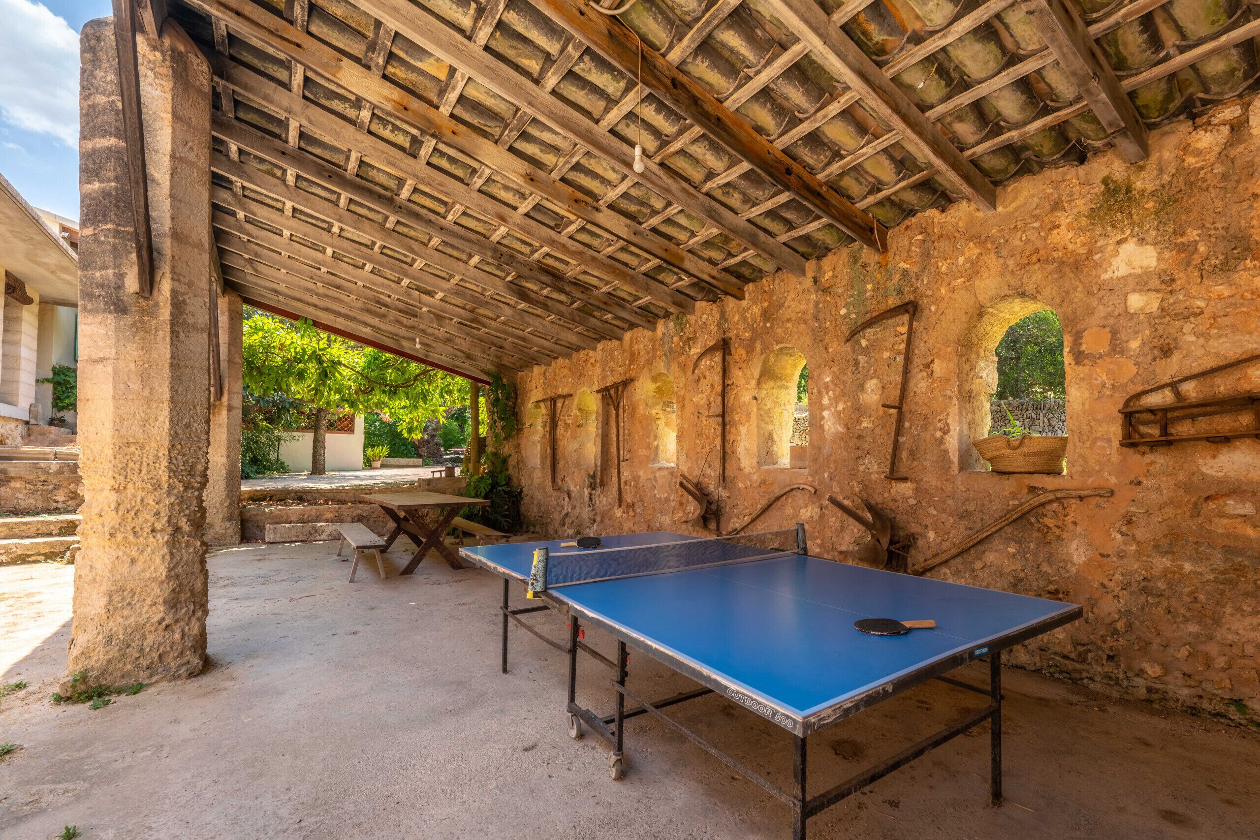 A ping pong table set up in an outdoor area with a rustic stone wall and wooden beams overhead.