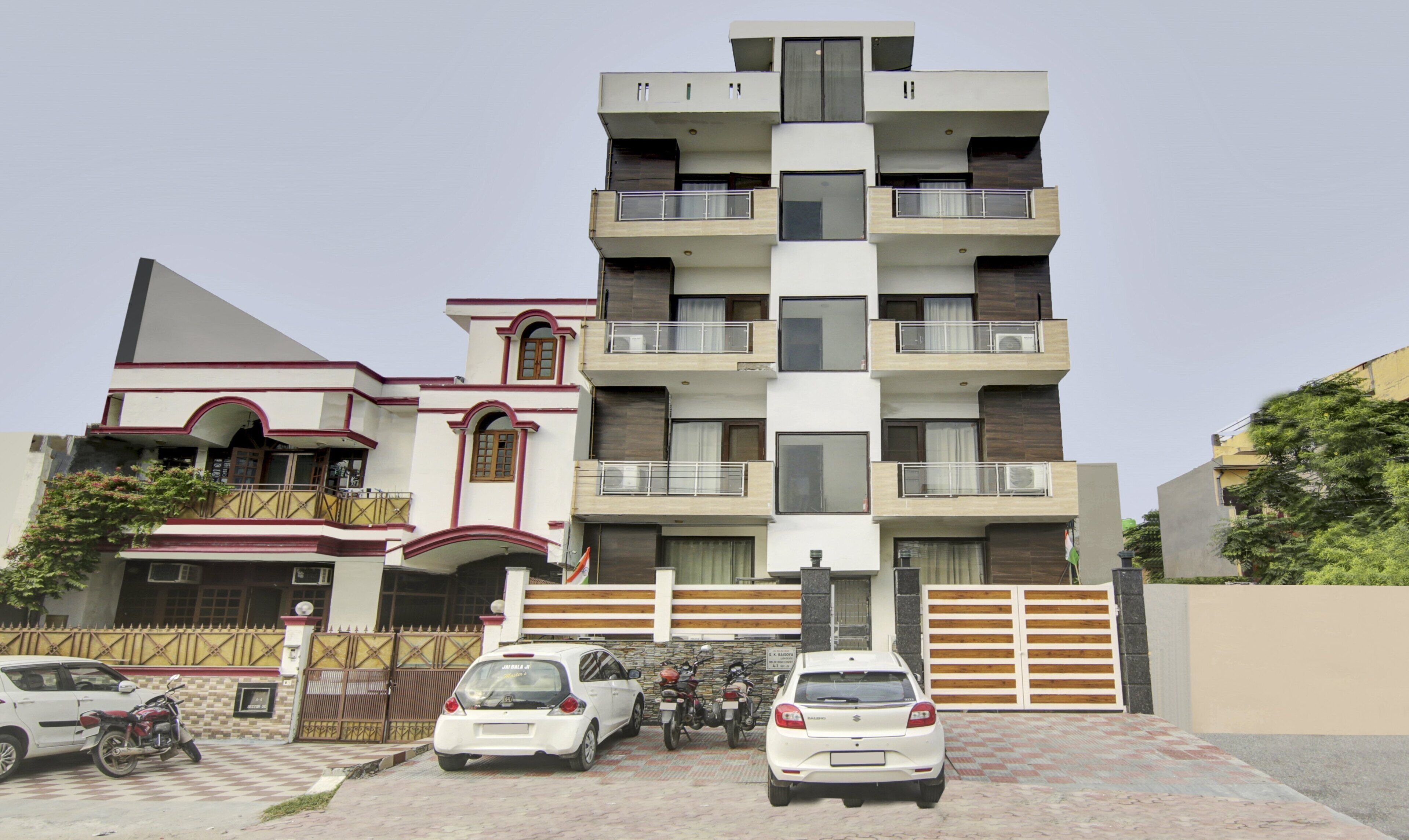 A multi-story residential building with balconies, a gated entrance, and parked vehicles.
