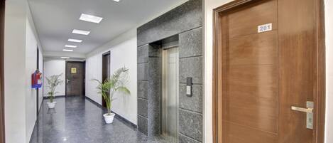 A hallway with a marble floor, a fire extinguisher, potted plants, an elevator, and a door marked with the number 201.