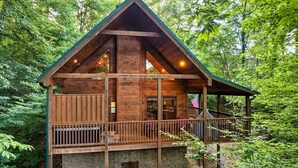 Eine Holzhütte mit einem Balkon, umgeben von dichtem Wald.