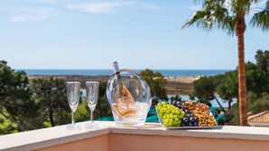 Een balkon met uitzicht op zee, een fles wijn, twee glazen en een schaal druiven en noten.