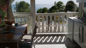 A balcony with a view of the sea, a dining table, chairs, and a kitchen area.