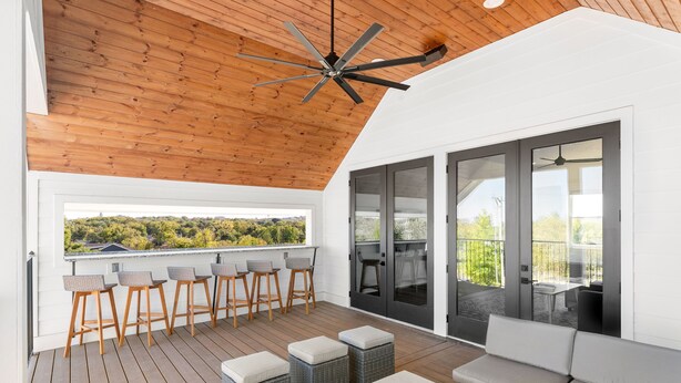 Un'area salotto all'aperto coperta, con pavimento in legno, ventilatore a soffitto e vista sul paesaggio.