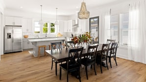 Una cucina moderna con mobili bianchi, un'isola centrale e un'area pranzo con sedie in legno.