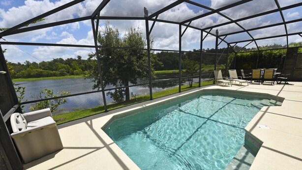 Une piscine rectangulaire à l’eau d’un bleu limpide, entourée d’une terrasse couverte avec des chaises et une table.