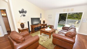 Un salon comprenant un ensemble de canapés, une table basse, un téléviseur et une vue sur une piscine, visible à travers une porte-fenêtre coulissante.