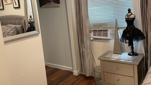 A bedroom with a bed, a nightstand, a dresser, a mirror, a window with curtains, and a wall-mounted air conditioner. - beautiful Modern apartment, close to everything ! (Hicksville)