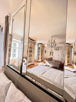 A bedroom with a large mirror reflecting the room's interior, including a bed, a sofa, and a chandelier. - AB Ljubljana - Breg Apartments (Ljubljana)